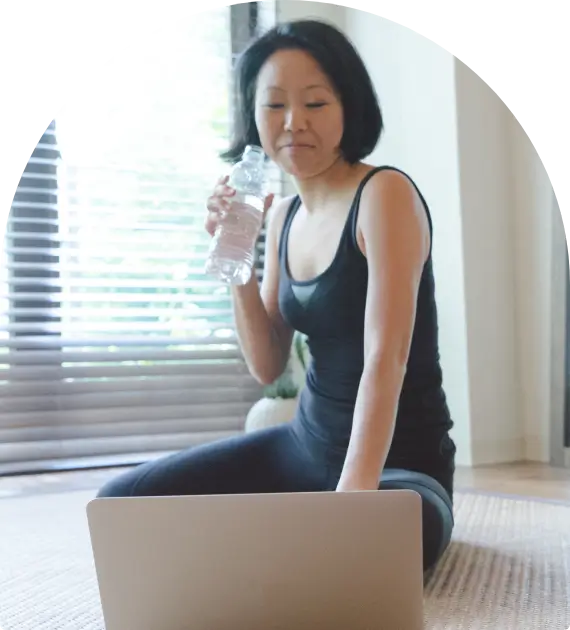 Woman sitting on the floor using a laptop and holding a glass of water.